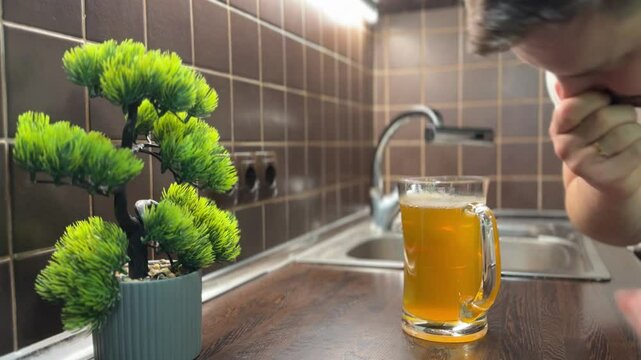 Man smells a beer glass filled with something rotten and instantly reacts to the strong odor. Taken in a kitchen with natural light and a humorous tone.