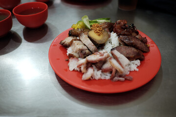 A diner enjoys a plate of Nasi Campur, a flavorful Peranakan Chinese-Indonesian dish featuring assorted roasted pork and egg, served in a bustling eatery