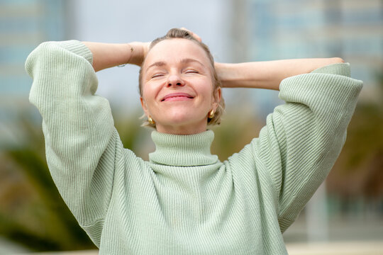Portrait of a happy woman with blond hair stretching with eyes closed and arms raised