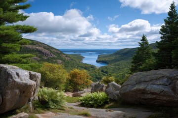 A scenic vista showcases a winding lake between wooded hills rocks in the foreground under a partly cloudy sky