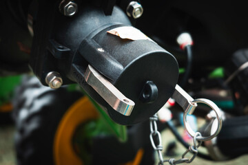 Agricultural trailer hitch with a metal safety pin attached by a chain, mounted on the rear of a vehicle.