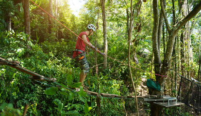 A man is walking across a challenging ropes course in the extreme park