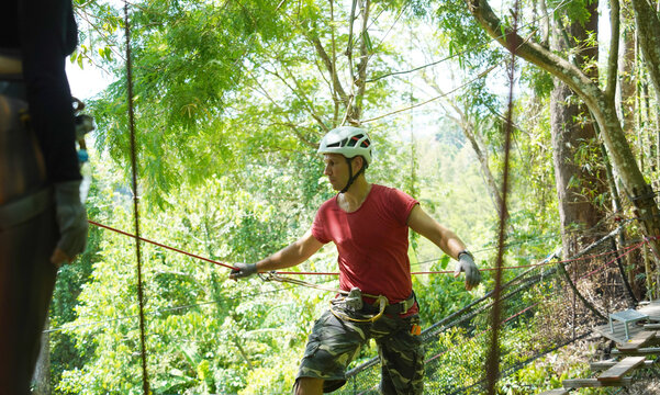 A man is walking across a challenging ropes course in the extreme park - Powered by Adobe