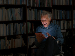 Man with surprised expression using a tablet in a home library