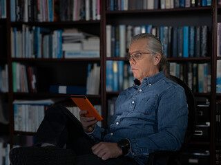 Man with scared expression holding an orange tablet in a library surrounded by books