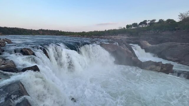Majestic Dhuandhar Falls at Bhedaghat flowing powerfully under a glowing sunset sky, capturing the serene beauty of nature in motion.