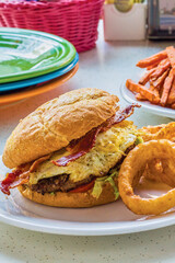 breakfast burger topped with lettuce, tomato, bacon, and a fried egg served with onion rings