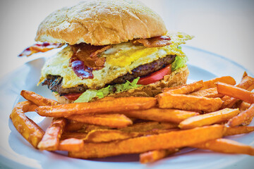 breakfast burger topped with lettuce, tomato, bacon, and a fried egg served with sweet potato fries