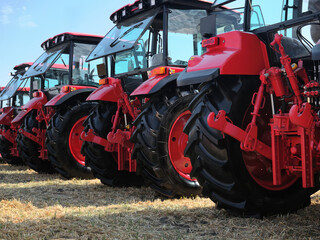 Rear view of several large modern red tractors standing in a field.