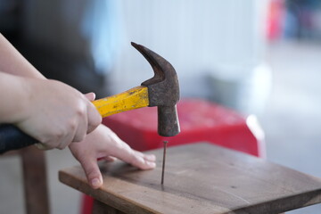 a person using a hammer to drive a nail into a wooden surface, with one hand holding the nail and the other gripping the hammer. This scene represents woodworking or DIY repair work