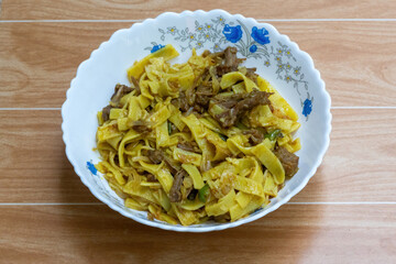 Homemade beef noodle dish in ceramic bowl, rustic wooden surface. Delicious comfort food.