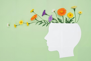 Mental Health Awareness Concept – White Paper Head Silhouette with Colorful Flowers on Green Background for Brain Health Education, World Brain Day Campaigns, and Wellness Advocacy