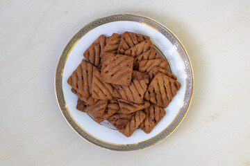Delicious Choco Chip Cookies on white plate, wooden surface. Premium square biscuits, top view....