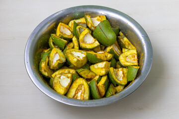 Green mango pieces with spices in steel bowl, ready for sun-drying. Natural food preservation for delicious pickle.