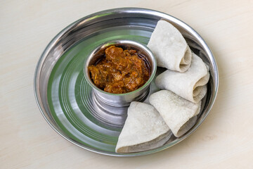 Spicy beef bhuna curry and fluffy roti in steel plate. A flavorful Bengali food, served on wood, juicy and ready for a tasty meal.