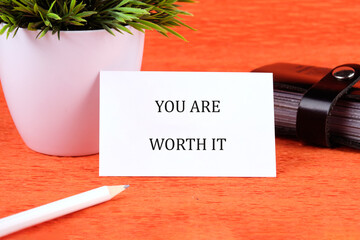 YOU ARE WORTH IT words written on a card next to a small potted plant and stationery