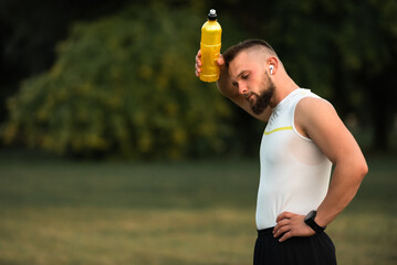 Tired male athlete or fit man cooling down with a water bottle after outdoor workout or run in the...