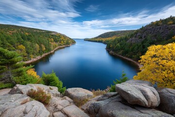 Deep blue lake scene bordered by rocky slopes and autumnal forests viewed from a rocky promontory Bright blue sky