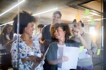 Group of diverse coworkers brainstorming ideas with sticky notes on glass wall