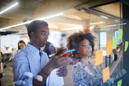 Group of diverse coworkers brainstorming ideas with sticky notes on glass wall