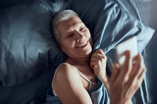 Senior woman smiling and taking a selfie in bed