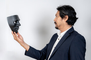 Male entrepreneur in formal suit holding dark mask as symbol of business fraud, scam, or deception.