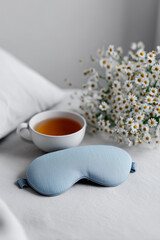 blue sleep mask, cup of tea, bouquet of flowers on the bed