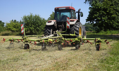 A tractor with a hay tedder at work in a agricultural field in the federal state of Brandenburg - Germany