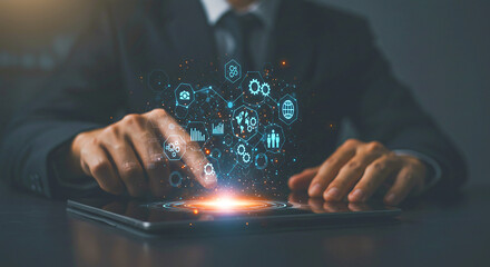 A person in a suit interacting with holographic icons above a tablet on a dark surface in a dim setting