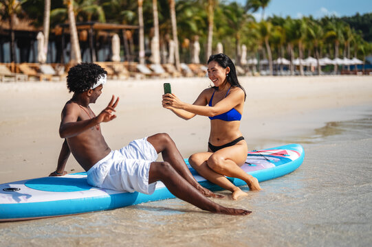 Diverse couple connected, embracing technology and social media while enjoying moments at the beach
