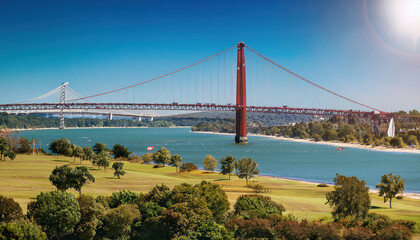 Stunning view of large red suspension bridge spanning river, surrounded by lush green trees and clear blue sky. scene captures beauty of nature