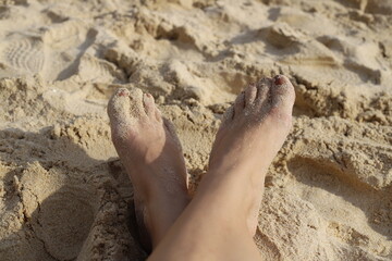 Bare feet covered with golden sand, resting on a beach under sunlight. A peaceful moment of relaxation and vacation by the sea.