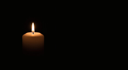 Solitary candle flame glowing in the darkness symbolizing hope and remembrance