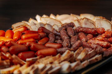 A close-up of a platter filled with various smoked sausages and sliced meats, featuring vibrant red and brown hues and rich textures.