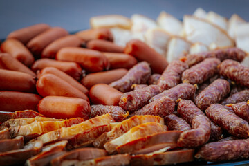 A close-up of a platter filled with various smoked sausages and sliced meats, featuring vibrant red and brown hues and rich textures.