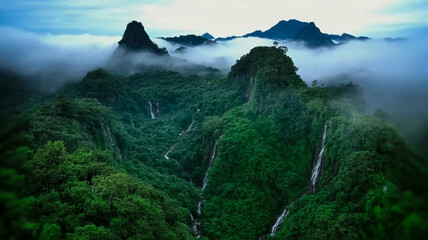 An aerial photograph of a lush green mountainous landscape shrouded in misty clouds.
