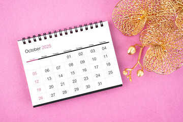 October 2025 desk calendar with golden orchid on pink background.