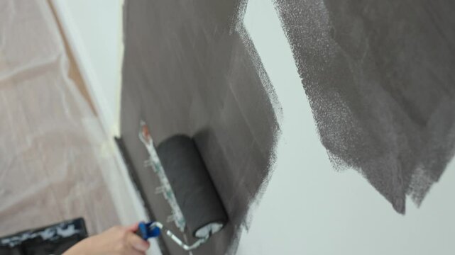 Detailed view of person using roller to paint wall black near electrical sockets during home renovation