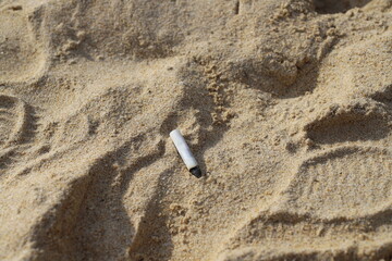 A discarded cigarette butt lies in the sand, symbolizing beach pollution and environmental neglect....