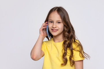 Little school girl on a white background in a yellow T-shirt, enthusiastically talking on the...