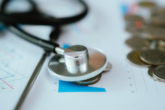 A stethoscope rests on financial charts and coins, suggesting the intersection of healthcare costs and economic analysis