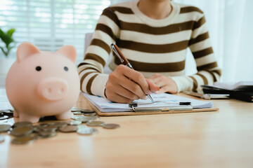 An Asian woman is putting money in a piggy bank while looking at a calculator, giving advice on financial planning.