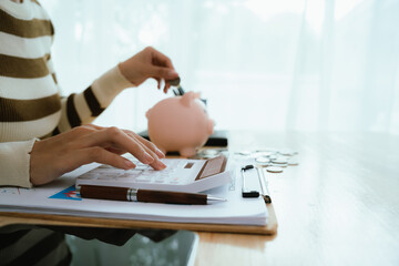 Fototapeta premium An Asian woman is putting money in a piggy bank while looking at a calculator, giving advice on financial planning.