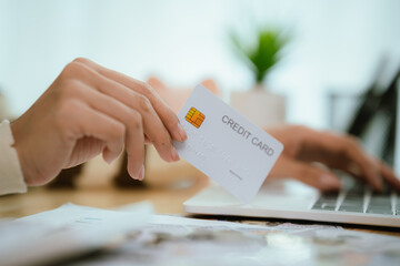 A person's hand holds a credit card over a laptop keyboard, indicating online shopping or payment transactions.