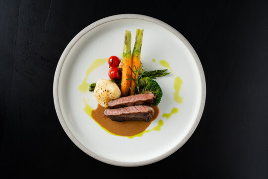 Grilled Steak with Roasted Vegetables and Brown Sauce on White Plate