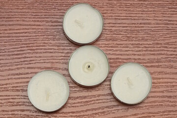 four white small decorative candles in a gray round metal box stand on a brown table