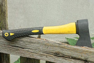 one big black yellow axe lies on the grey board of an old fence on a rural street