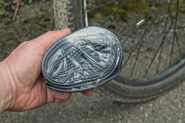 hand holding one black rubber bicycle tube in package against background of bicycle wheel on summer...