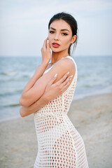 Portrait of alluring young woman in white dress on the sea coast. Beautiful girl on the beach