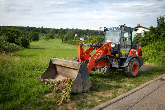 Ein Radlader der Marke Kubota R070 steht mit fehlendem linken Vorderrad auf einer Wiese am Strassenrand